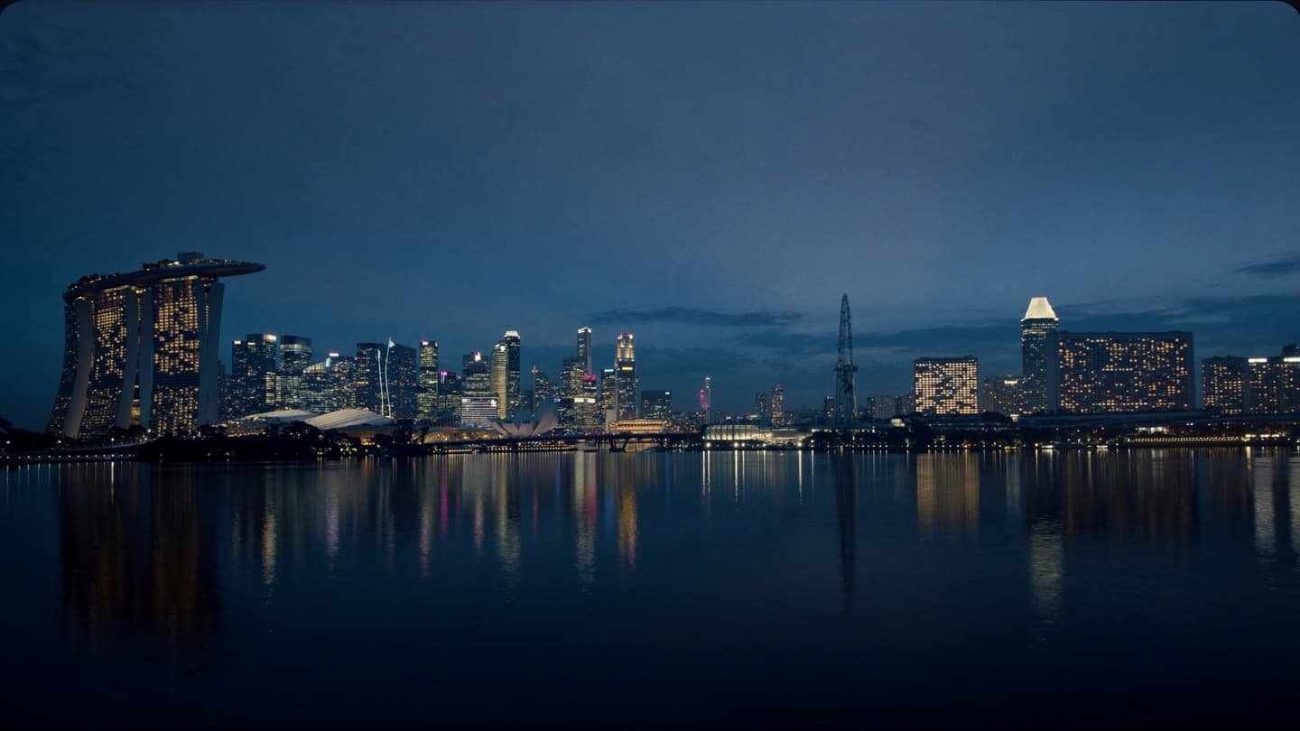 The Marina Bay skyline at blue hour, seen across still water from the far side of the bay.